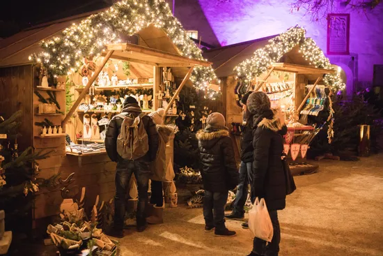 People shopping at wooden stalls decorated with Christmas lights at a festive market